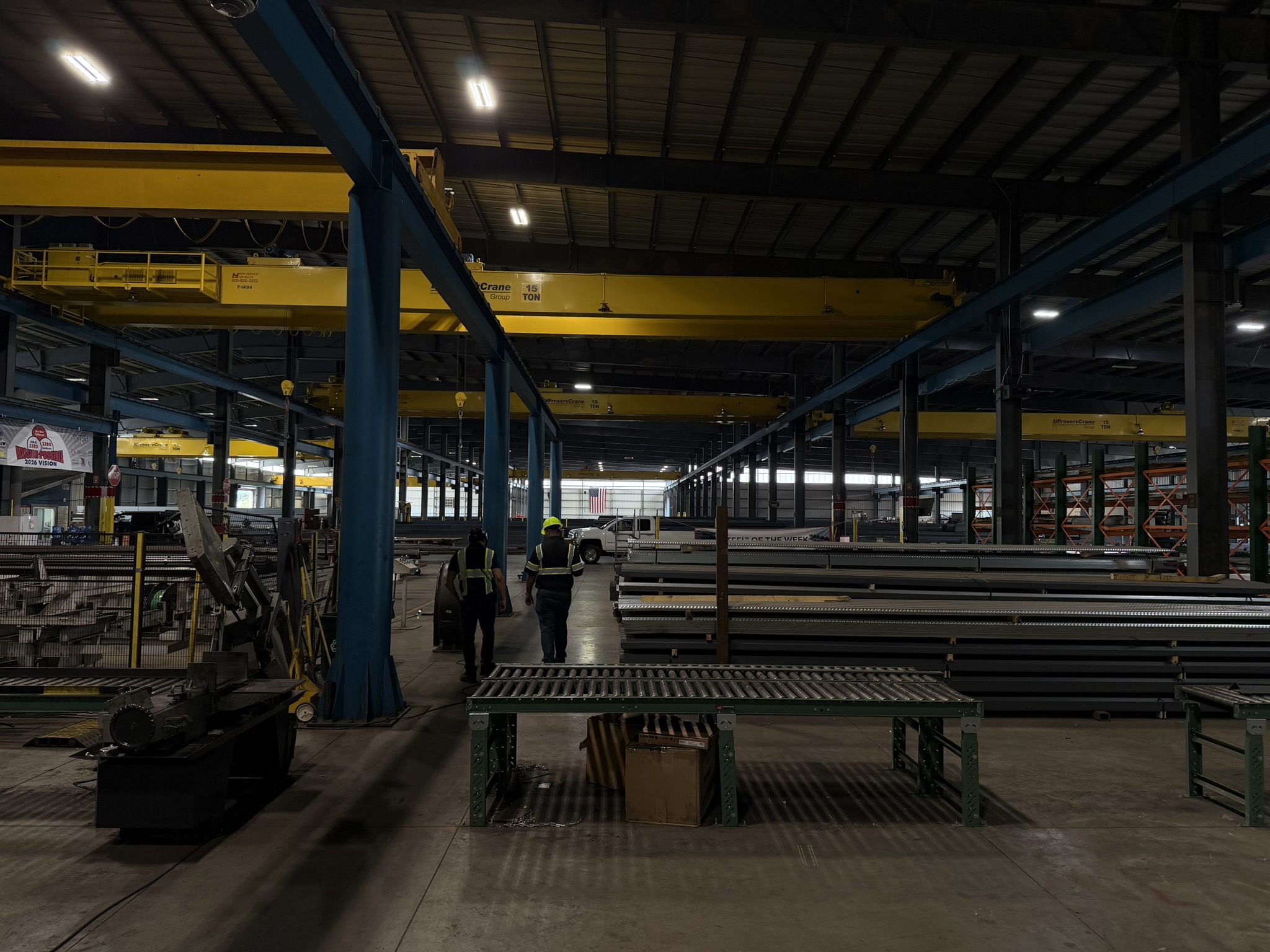 Factory bay with overhead cranes and staged steel stock; annotations identify the crane span and stock